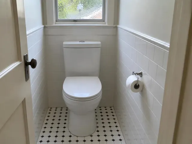 Clean white toilet in a small tiled bathroom with frosted window and patterned floor in Gladesville